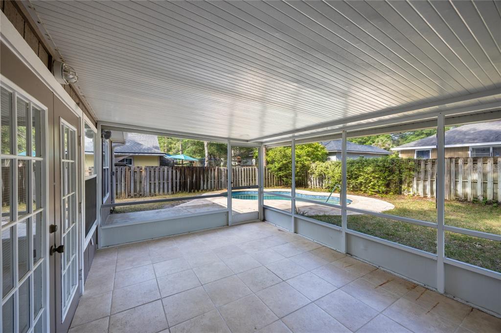 A screened-in patio with tiled flooring overlooks a backyard swimming pool and wooden fence — 4511 NW 35TH STREET, GAINESVILLE, FL