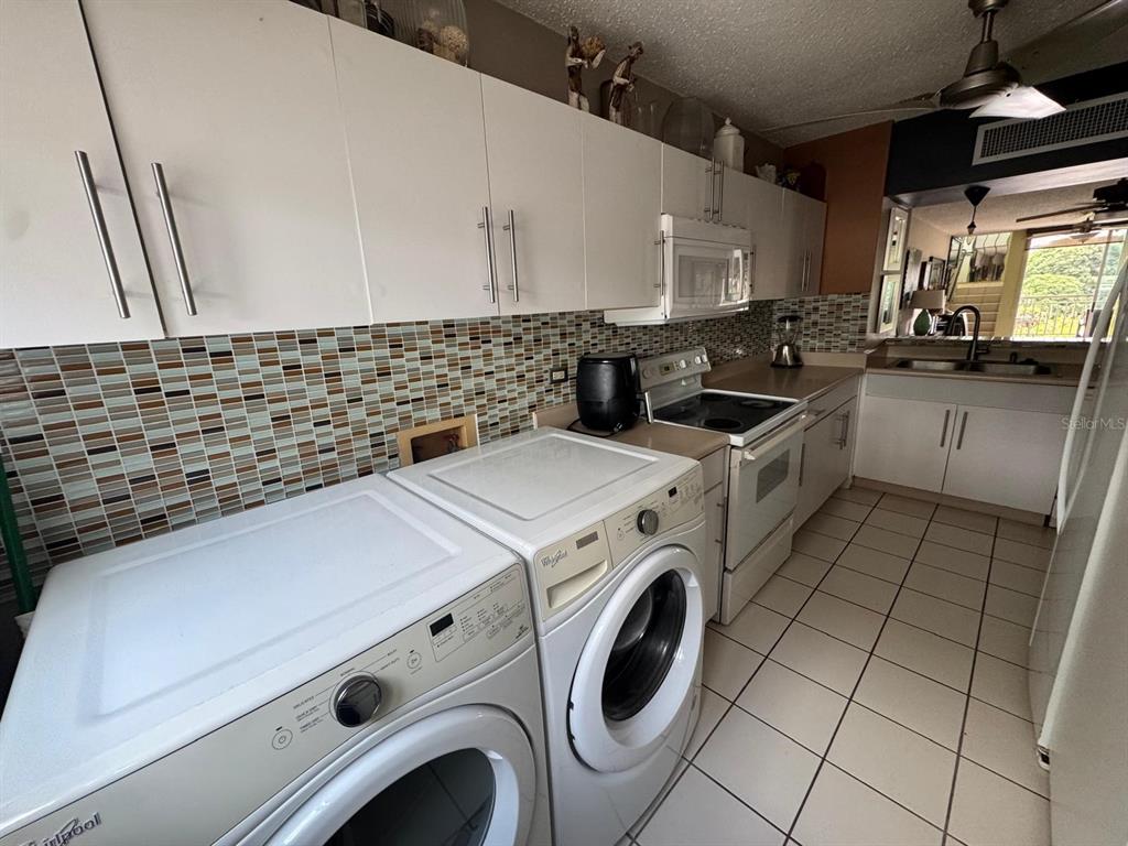 A kitchen features white cabinets, a tiled backsplash, and a side-by-side washer and dryer — Carr. 199 PASEO DEL BOSQUE UNIT 3-507, SAN JUAN, PR