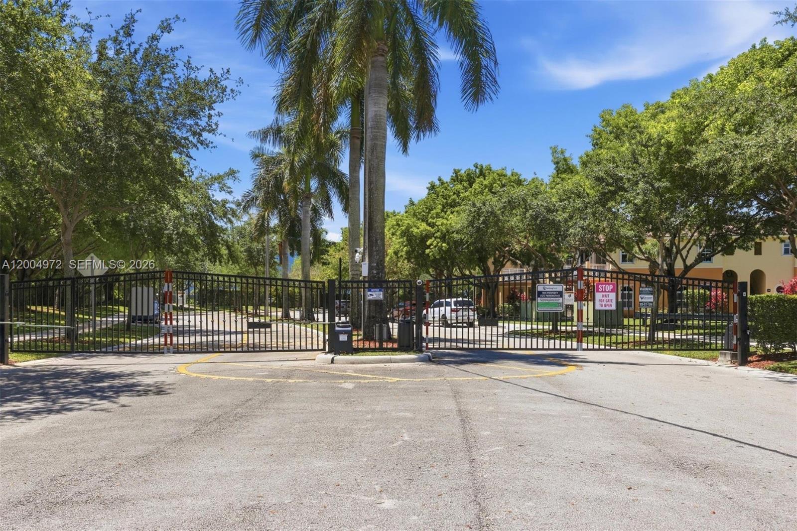A gated entrance with palm trees and lush landscaping leads into a residential community — 10012 NW 7th St # 209, Miami FL 33172, MIAMI, FL