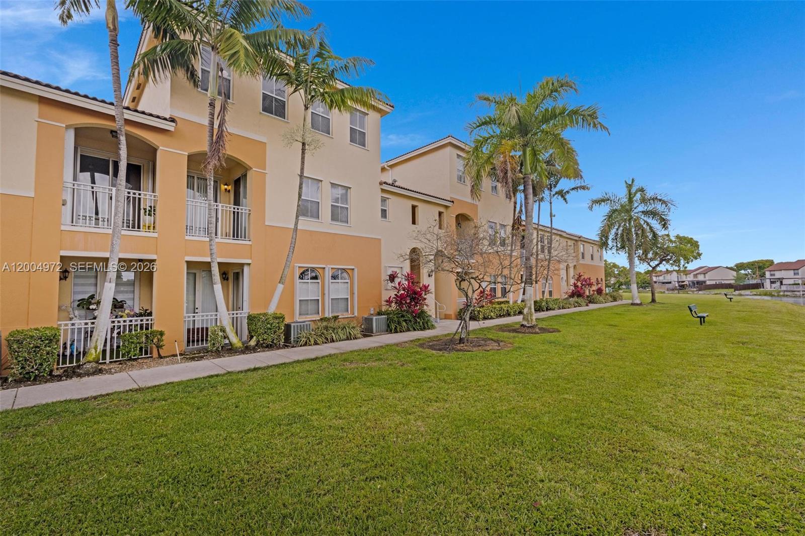 A multi-story apartment building with yellow stucco walls sits beside a grassy lawn — 10012 NW 7th St # 209, Miami FL 33172, MIAMI, FL