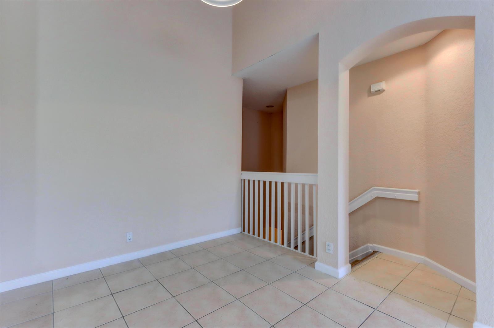 An interior view showing a tiled landing with a white railing overlooking a staircase — 3061 Laurel Ridge Circle, Riviera Beach FL 33404, RIVIERA BEACH, FL