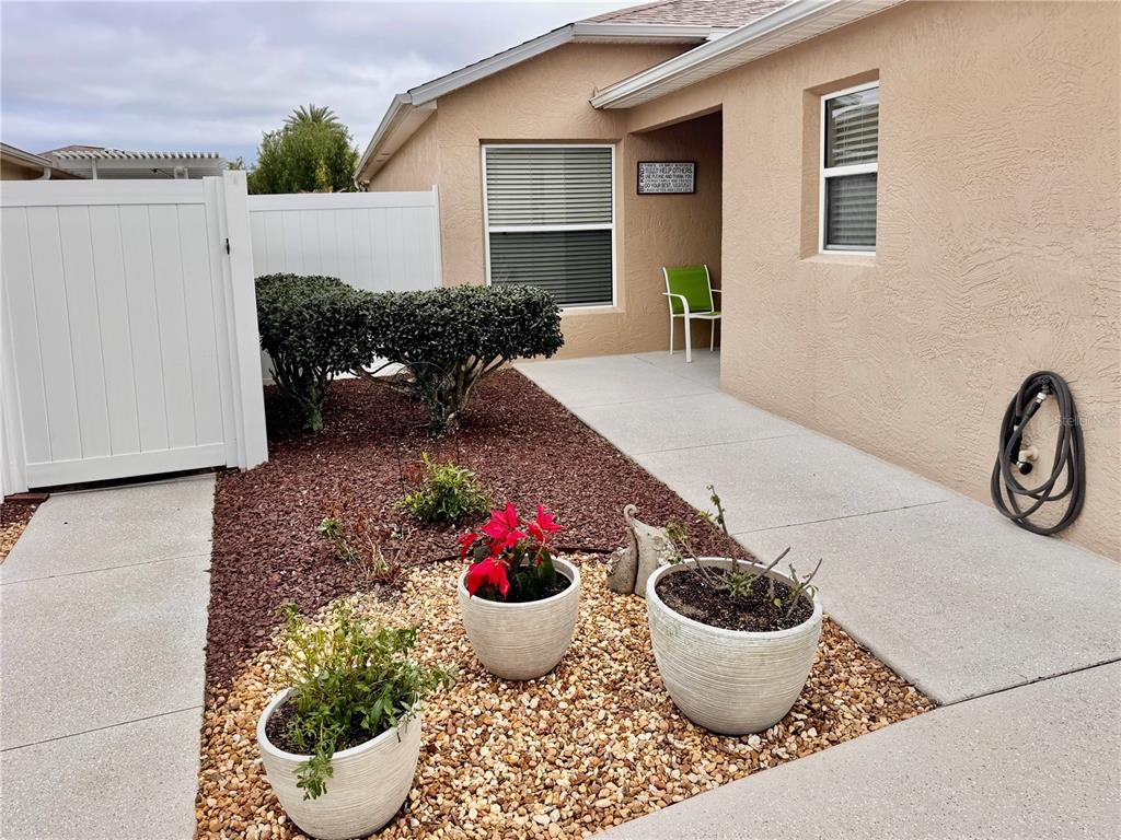 A tan house exterior features a concrete walkway, potted plants, and a white privacy fence — 2000 GOLDENROD COURT, THE VILLAGES, FL