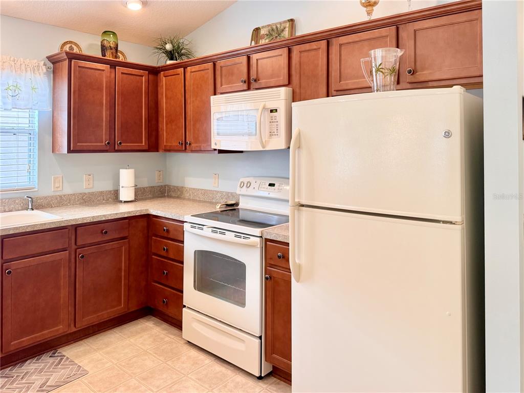 A kitchen features wood cabinets, white appliances, and light-colored countertops — 2000 GOLDENROD COURT, THE VILLAGES, FL