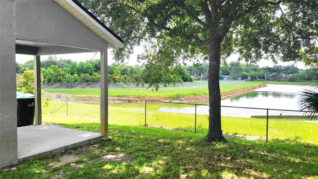 A covered concrete patio overlooks a grassy yard, a chain-link fence, and a pond — 3871 CLUBSIDE POINTE DRIVE, ORLANDO, FL