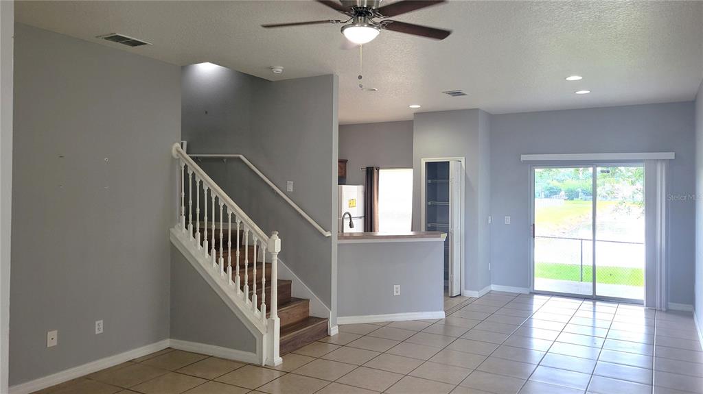 An open-concept living area features a staircase, tile flooring, and sliding glass doors to outside — 3871 CLUBSIDE POINTE DRIVE, ORLANDO, FL