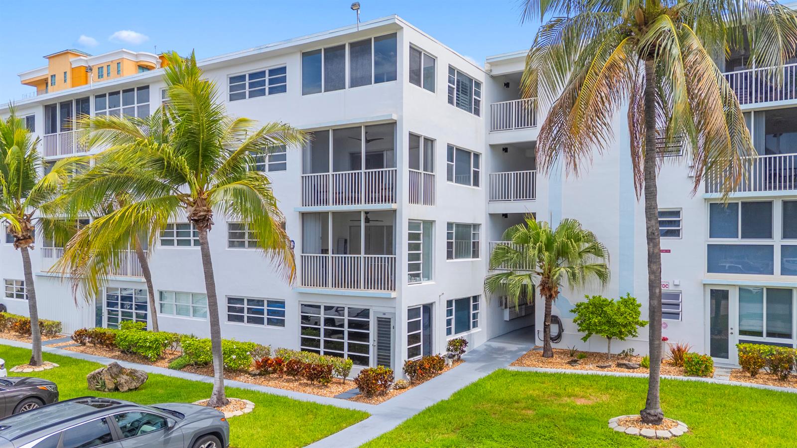 A multi-story white apartment building with screened balconies and palm trees in the foreground — 3201 NE 8th Street # 206, Pompano Beach FL 33062, POMPANO BEACH, FL