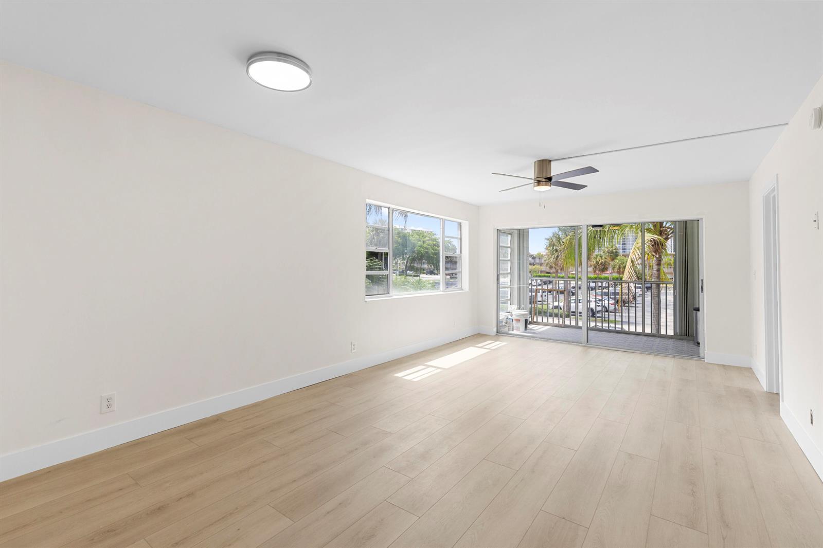 An empty room features light wood-look flooring, a ceiling fan, and a sliding glass door — 3201 NE 8th Street # 206, Pompano Beach FL 33062, POMPANO BEACH, FL