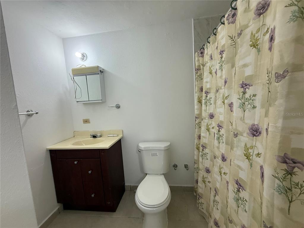 A bathroom features a dark wood vanity, a white toilet, and a floral shower curtain — 223 ALMENDRO, JUANA DIAZ, PR