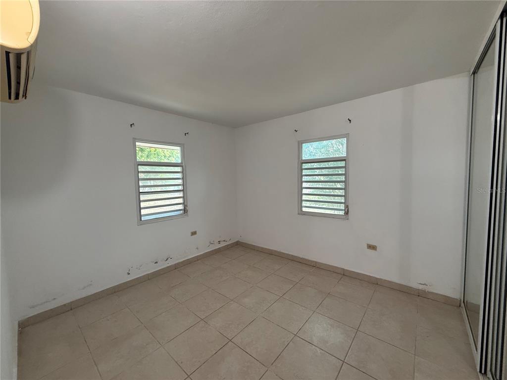 An empty bedroom features white walls, tiled flooring, two louvered windows, and a sliding closet door — 223 ALMENDRO, JUANA DIAZ, PR