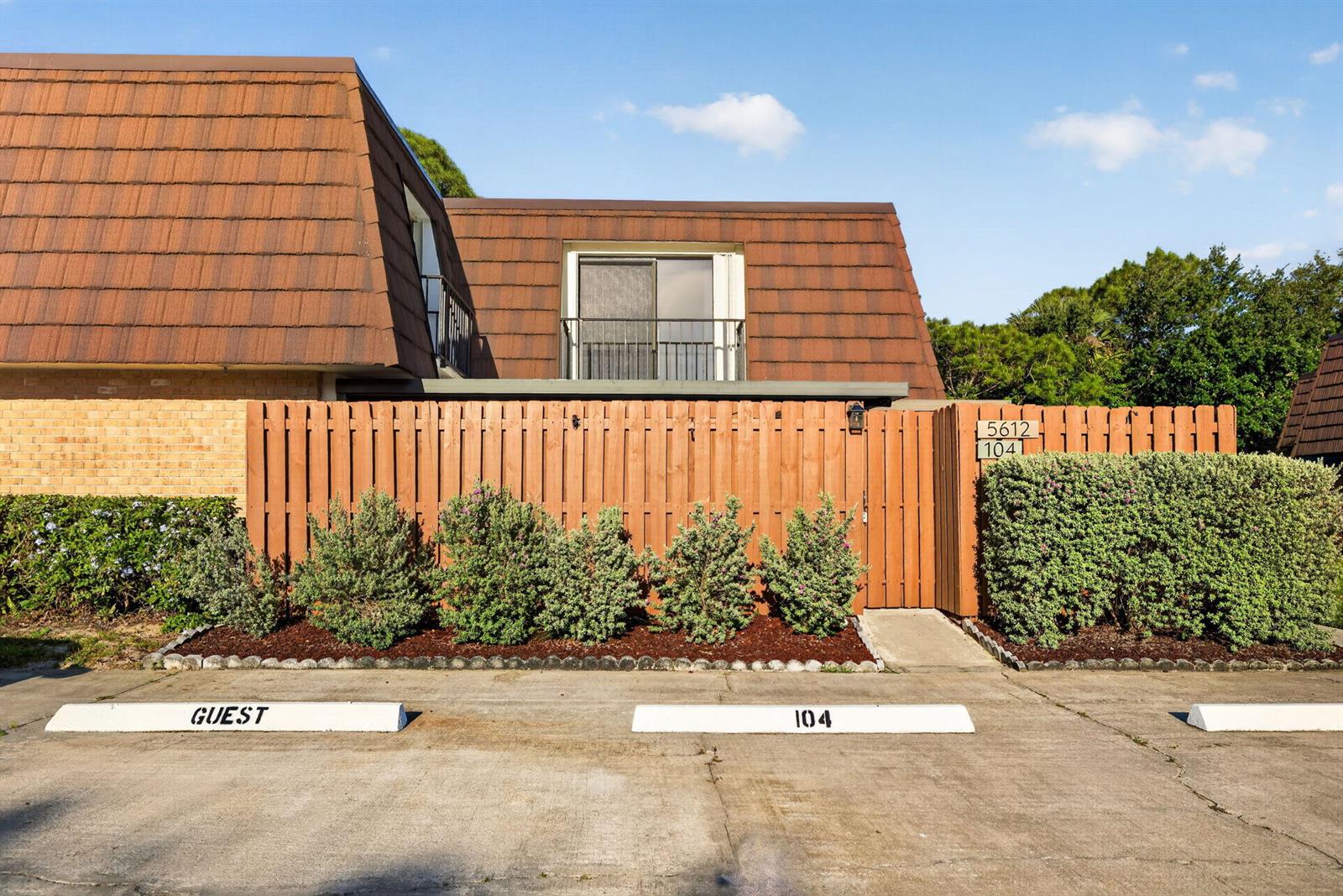 A two-story building exterior features a brown mansard roof, a wooden privacy fence, and parking — 5612 SE Riverboat Drive # 104, Stuart FL 34997, STUART, FL