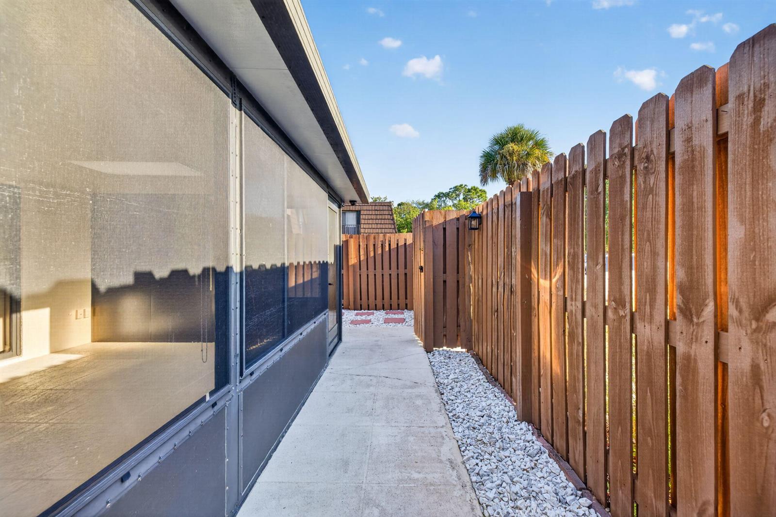 A concrete walkway runs between a screened-in porch and a tall wooden privacy fence — 5612 SE Riverboat Drive # 104, Stuart FL 34997, STUART, FL
