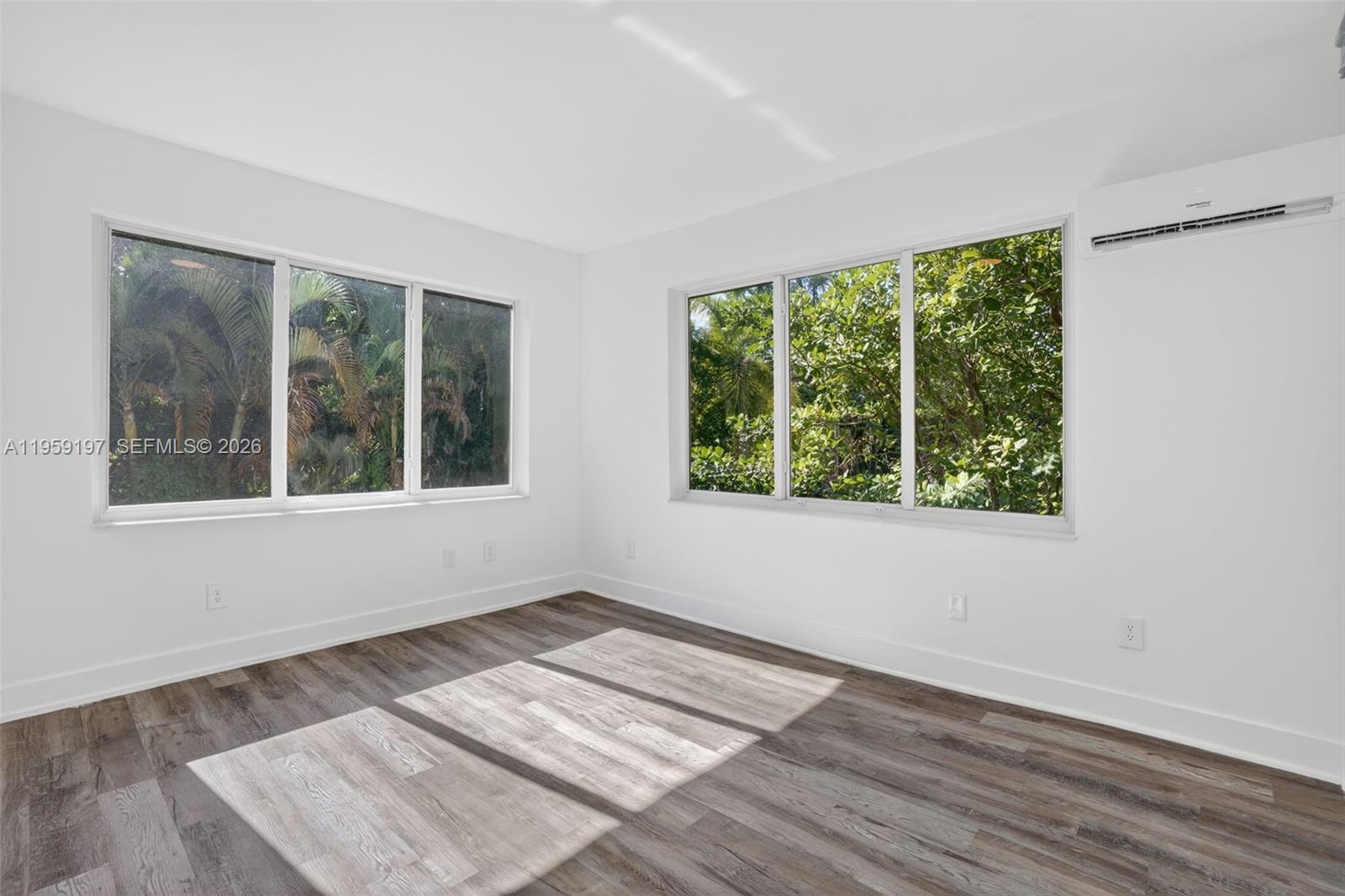 An empty room with white walls, wood-look flooring, large windows, and a wall-mounted air conditioner — 1630 SW 10th St, Miami FL 33135, MIAMI, FL