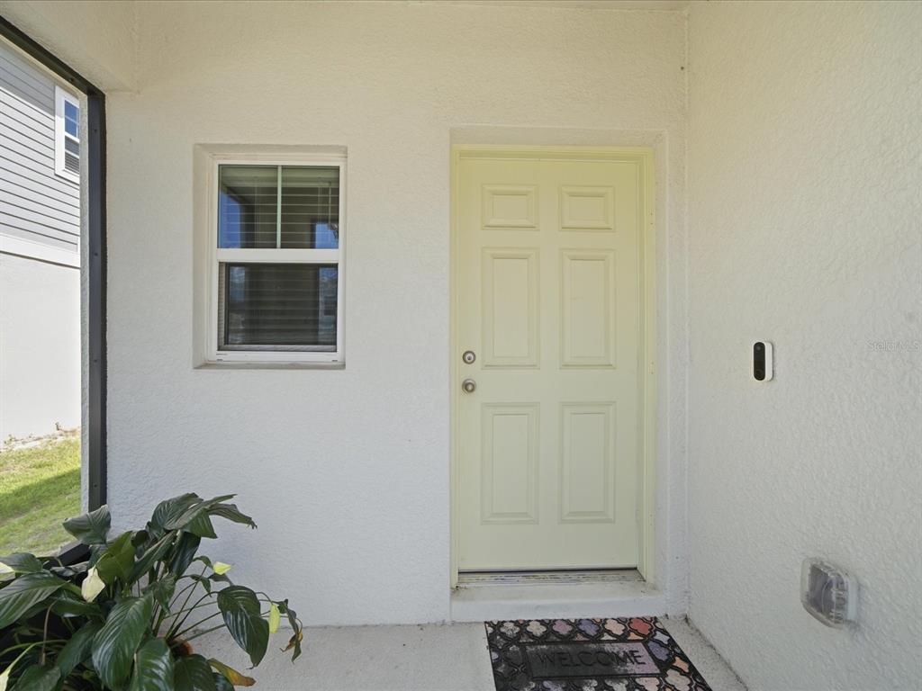 A light-colored front door with a window and a welcome mat on a porch — 34149 SCARLET SAGE COURT, WESLEY CHAPEL, FL