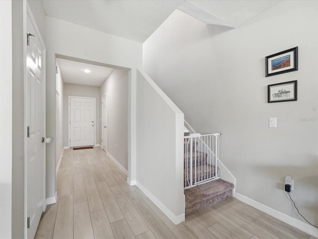 A hallway with light wood-look flooring leads to a front door near carpeted stairs — 34149 SCARLET SAGE COURT, WESLEY CHAPEL, FL