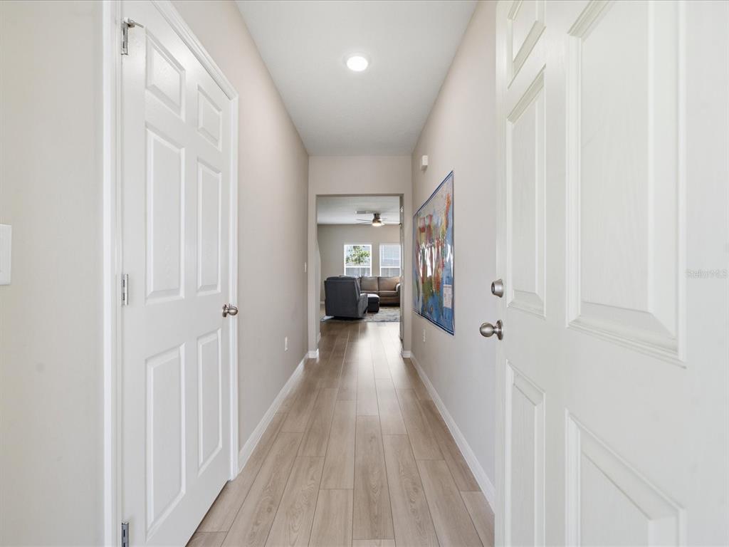 A hallway with light wood-look flooring leads toward a living room with a sofa — 34149 SCARLET SAGE COURT, WESLEY CHAPEL, FL