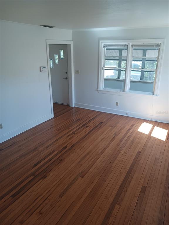 An empty room with hardwood floors, white walls, and a window looking onto a porch — 3720 4TH AVENUE N, ST PETERSBURG, FL