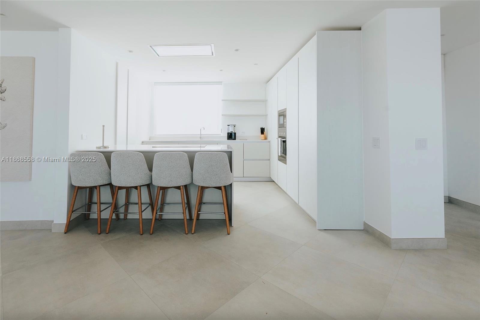 A modern kitchen features white cabinetry, a central island with four barstools, and tile flooring — 1 Irausquin Blvd Eagle beach Aruba # 4B, Ar, Ar