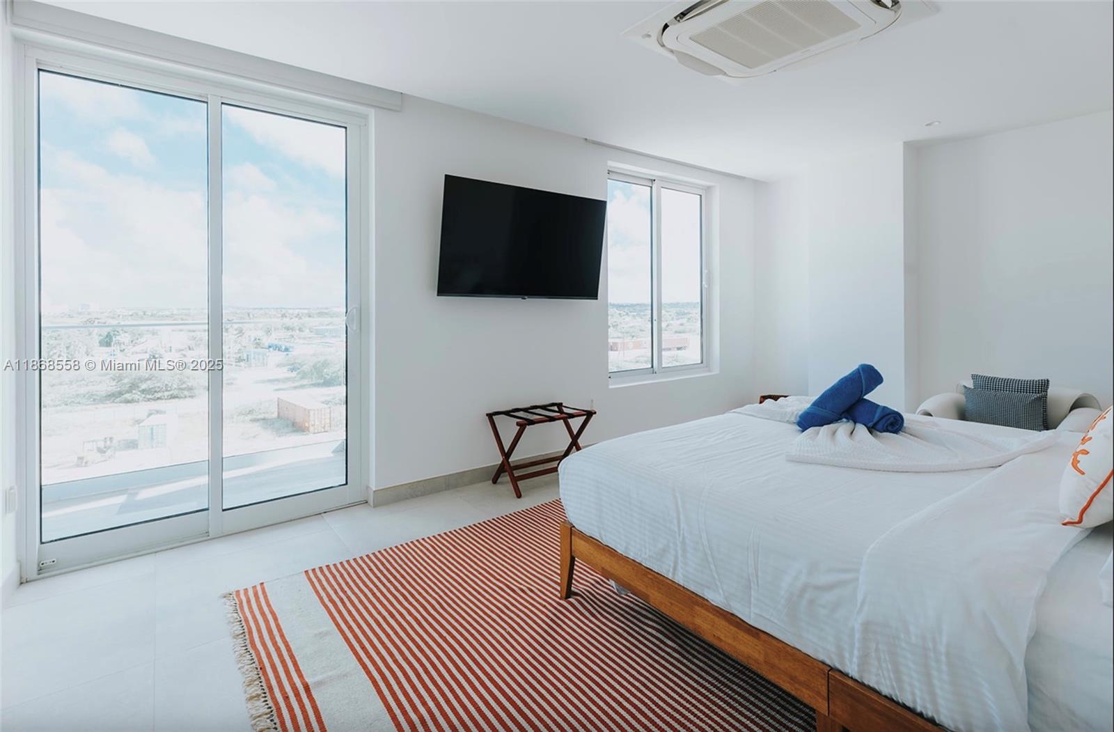 A bedroom features a bed, a wall-mounted television, a striped rug, and a balcony view — 1 Irausquin Blvd Eagle beach Aruba # 4B, Ar, Ar