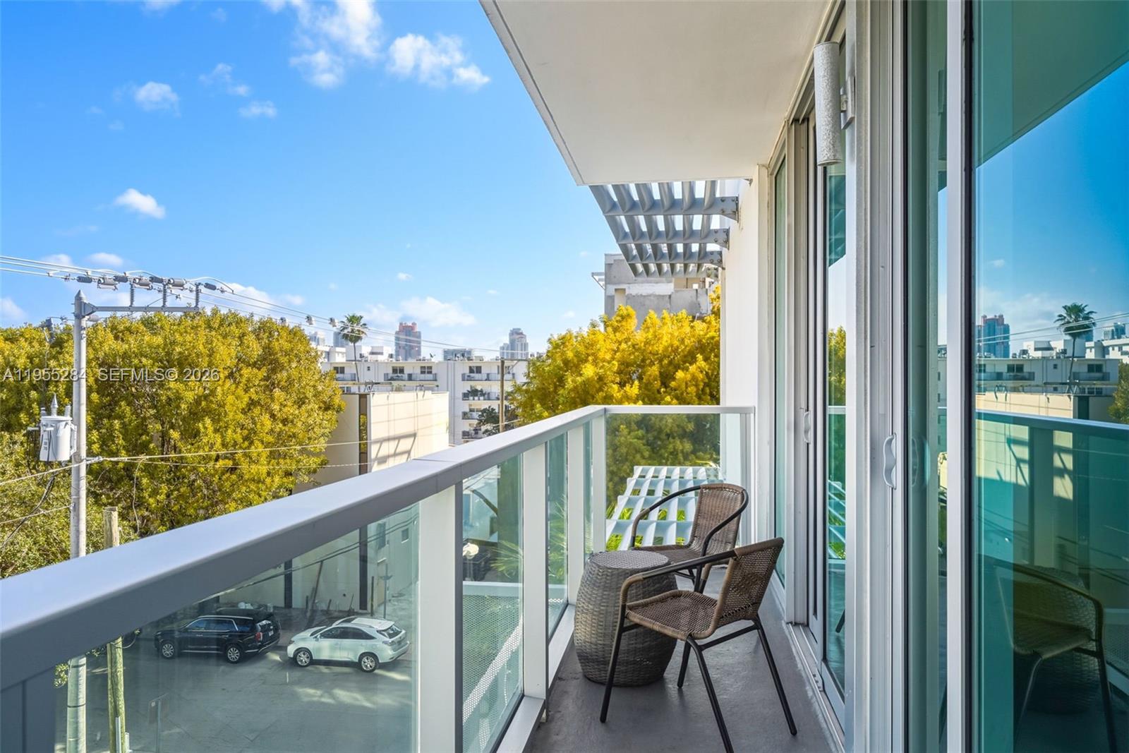 A balcony with glass railings, two wicker chairs, and a small table overlooks a parking lot — 1215 West Ave # 408, Miami Beach FL 33139, MIAMI BEACH, FL