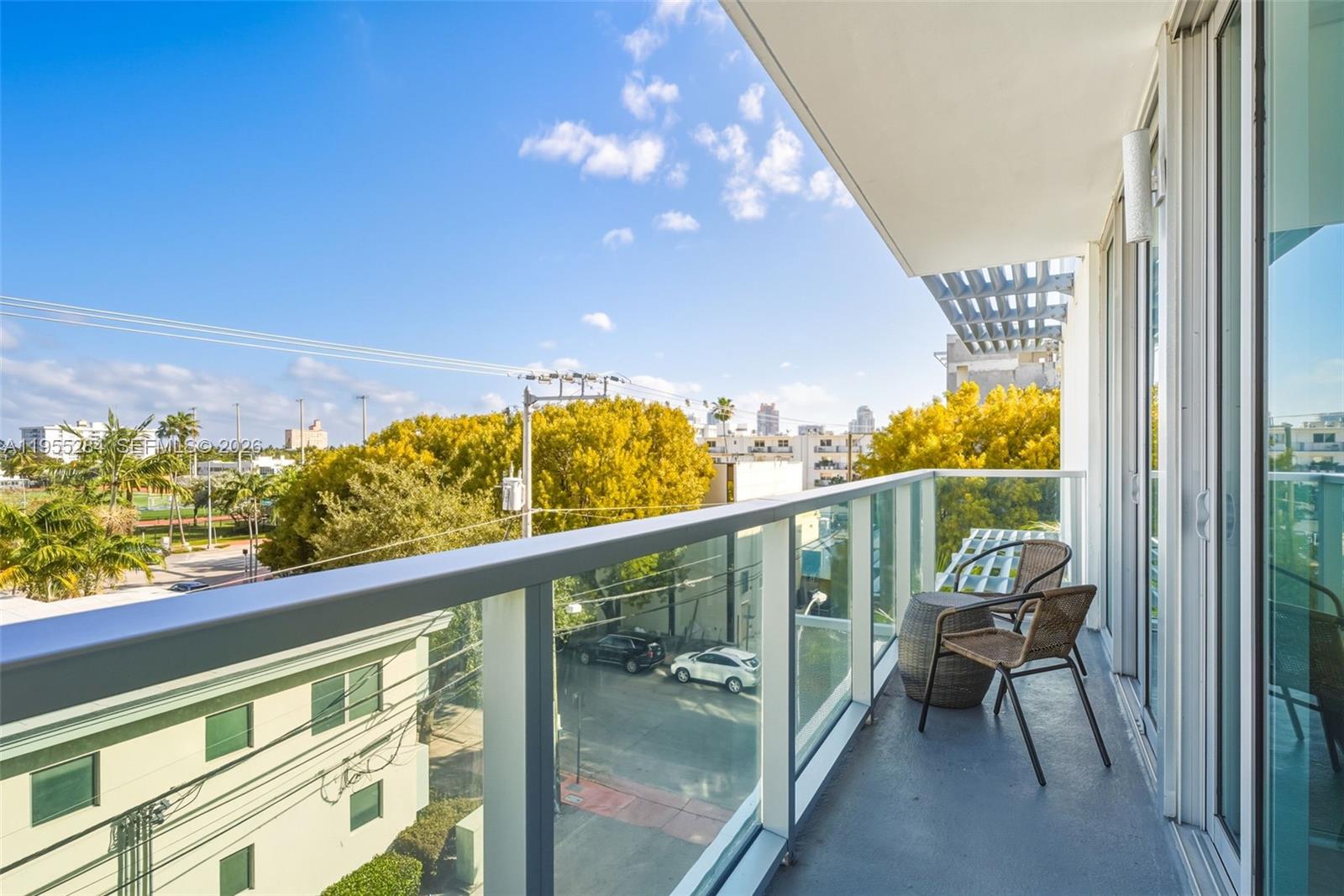 A balcony with a glass railing features two wicker chairs and a small side table — 1215 West Ave # 408, Miami Beach FL 33139, MIAMI BEACH, FL