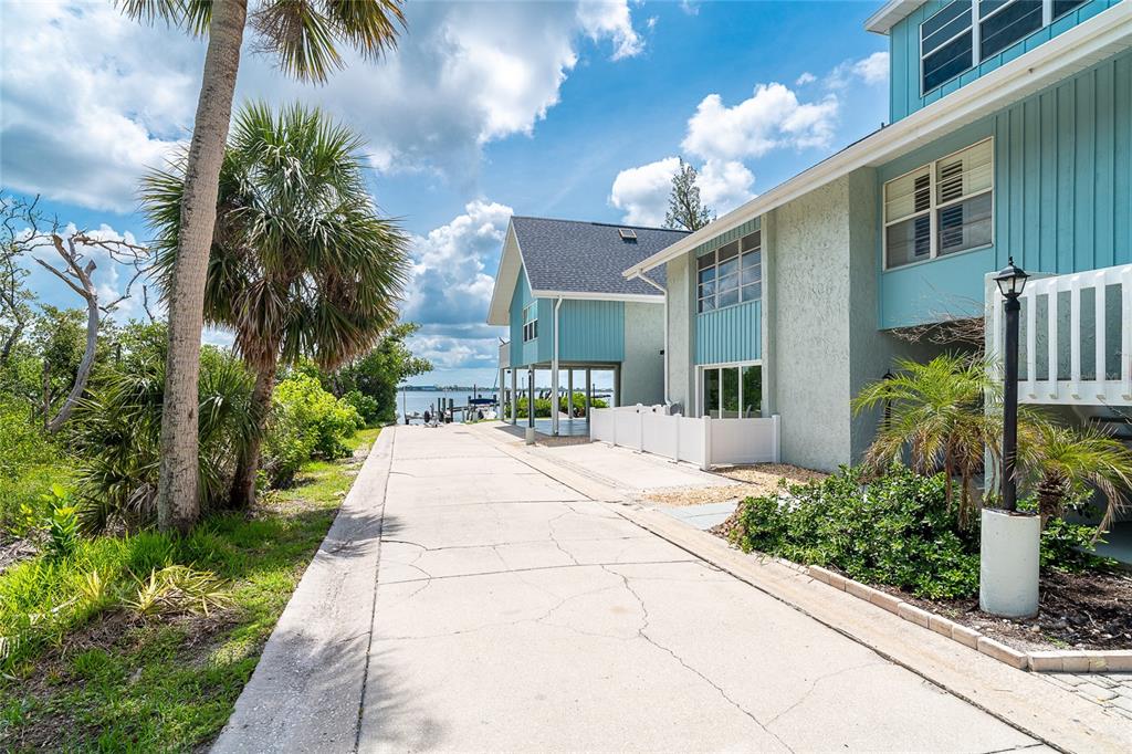 A concrete driveway leads toward a waterfront house with blue siding and a palm tree — 6005 N BEACH ROAD UNIT 16, ENGLEWOOD, FL
