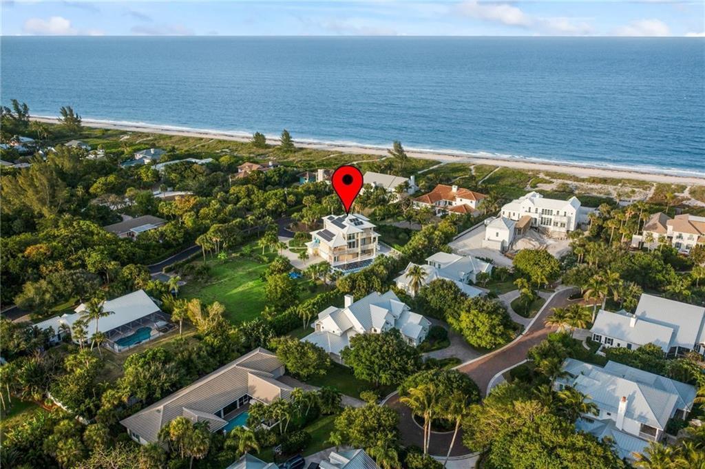 An aerial view shows a multi-story house with solar panels near a beach and ocean — 2275 Genesea Lane, Vero Beach FL 32963, VERO BEACH, FL