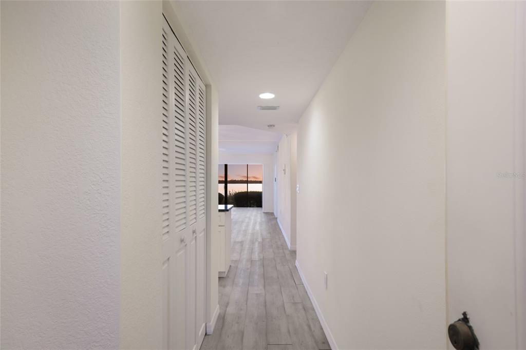 A hallway with light wood-look flooring leads to a living area with a large window — 4761 INDEPENDENCE DRIVE UNIT 4761, BRADENTON, FL