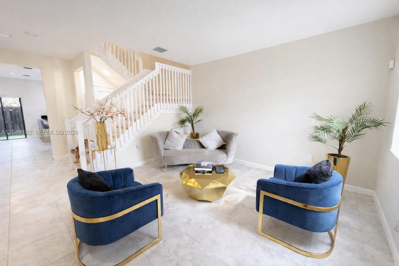 A living room features a staircase, two blue velvet chairs, a sofa, and a gold table — 323 NE 208th Ter # 0, Miami FL 33179, MIAMI, FL