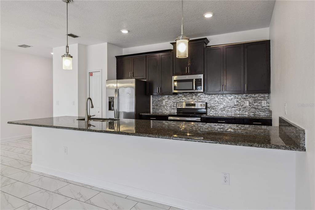 A kitchen with dark cabinets, granite countertops, a breakfast bar with stools, and stainless appliances — 1584 SLICE WAY, DAVENPORT, FL