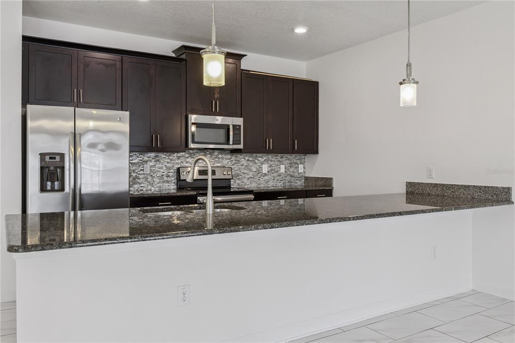 A kitchen features dark wood cabinets, granite countertops, stainless steel appliances, and a breakfast bar — 1584 SLICE WAY, DAVENPORT, FL