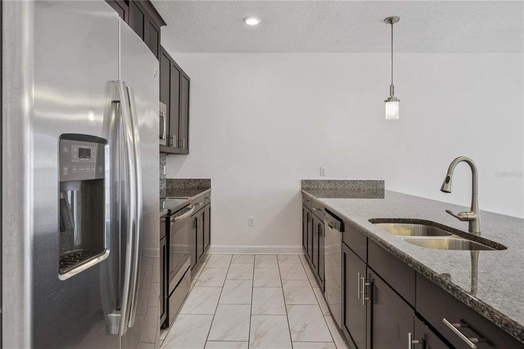 A kitchen features dark wood cabinets, granite countertops, stainless steel appliances, and a breakfast bar — 1584 SLICE WAY, DAVENPORT, FL