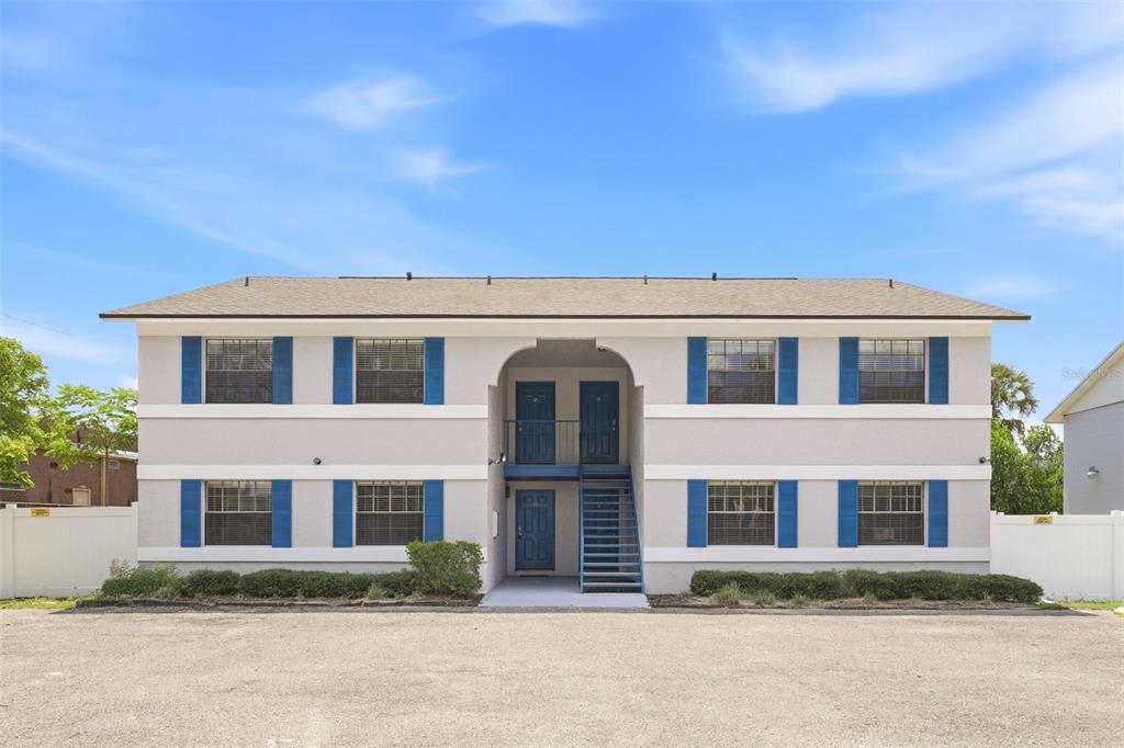 A two-story apartment building with a central staircase and blue shutters against a gravel lot — 10 N FAIRFAX AVENUE UNIT 10, WINTER SPRINGS, FL