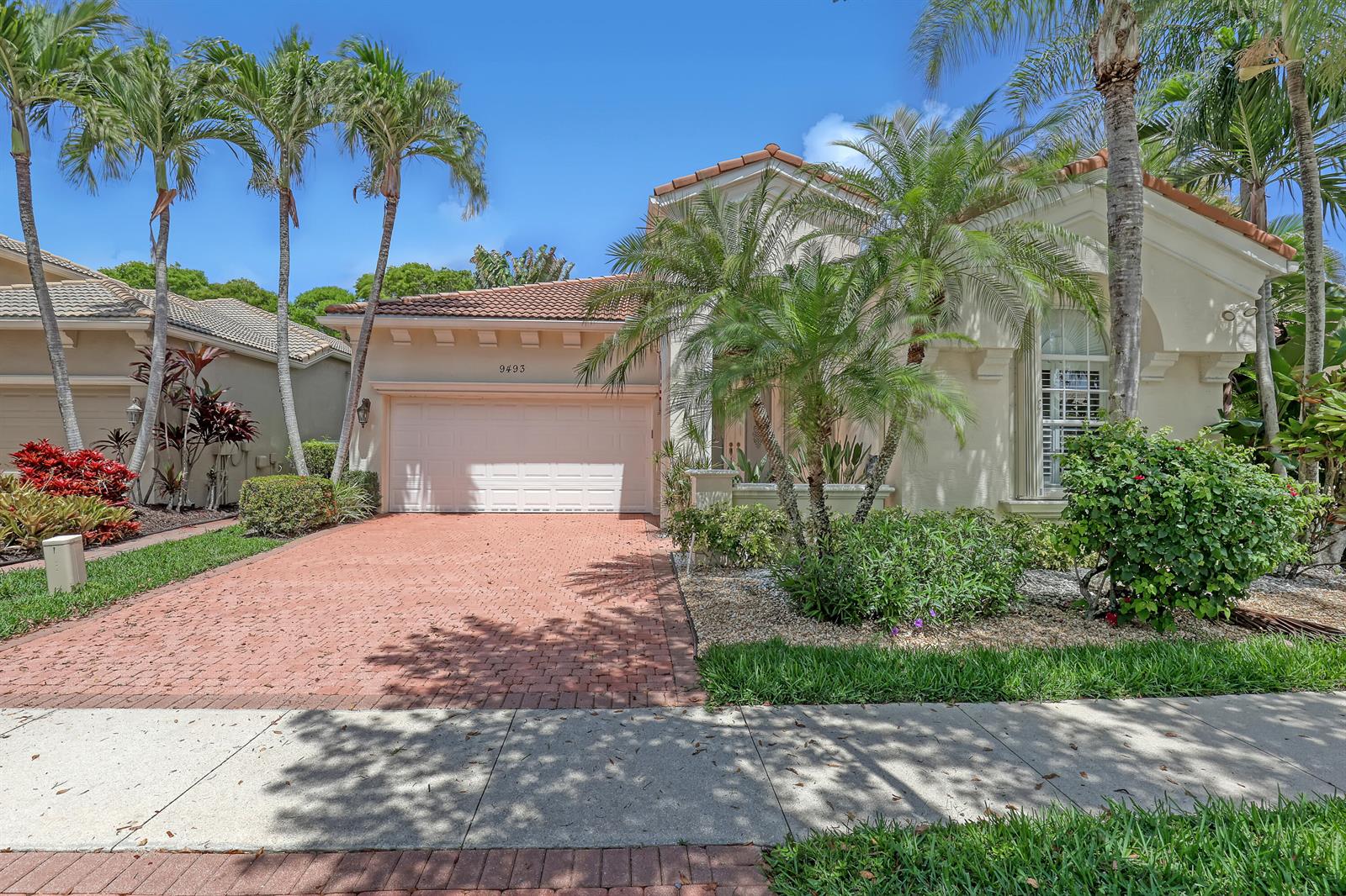 A single-story house with a brick driveway, a two-car garage, and surrounding palm trees — 9493 Via Elegante, Wellington FL 33411, WELLINGTON, FL