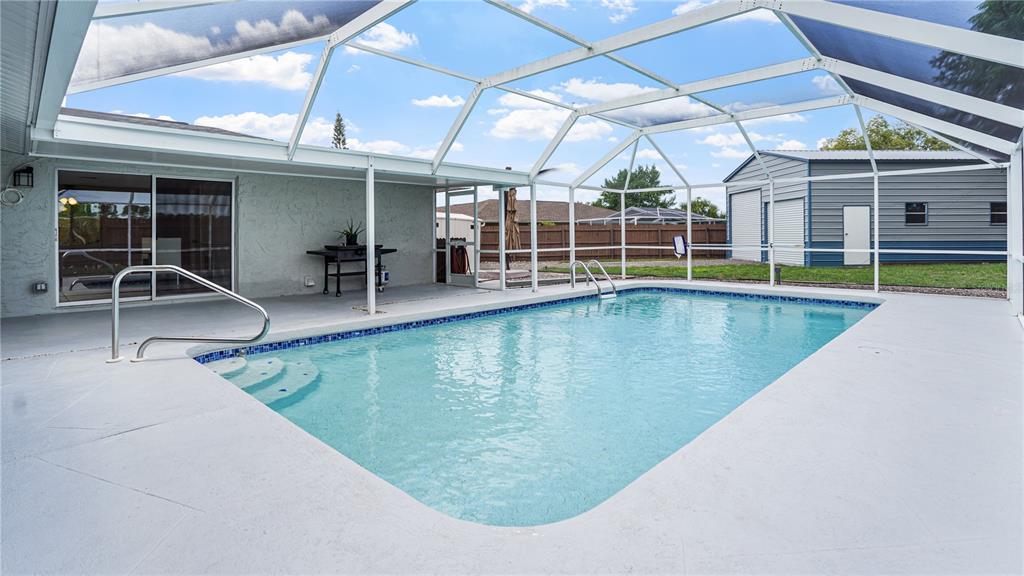A screened-in swimming pool with a concrete patio and a detached garage in the background — 8747 HEMLOCK LANE, PORT RICHEY, FL