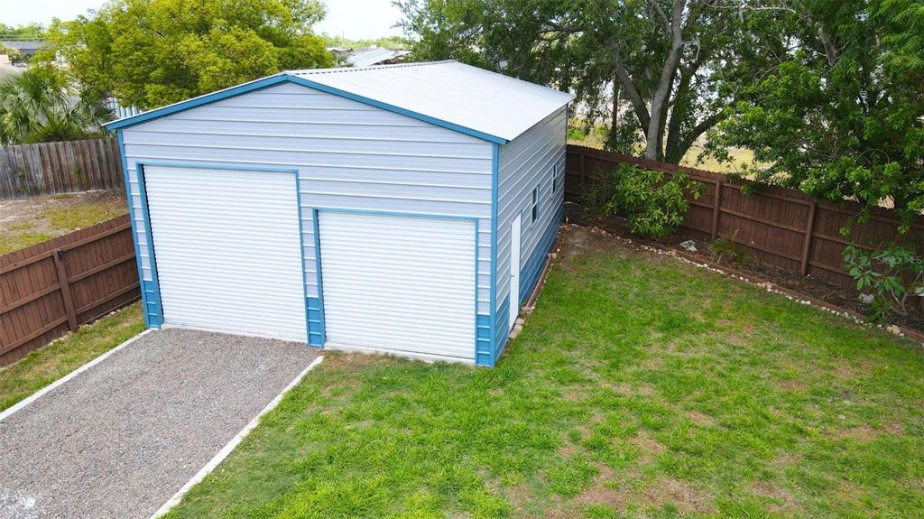A detached metal garage with two roll-up doors sits in a fenced backyard — 8747 HEMLOCK LANE, PORT RICHEY, FL