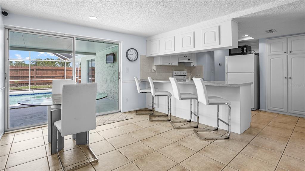 A kitchen with white cabinets, a breakfast bar, and a dining area overlooking a pool — 8747 HEMLOCK LANE, PORT RICHEY, FL