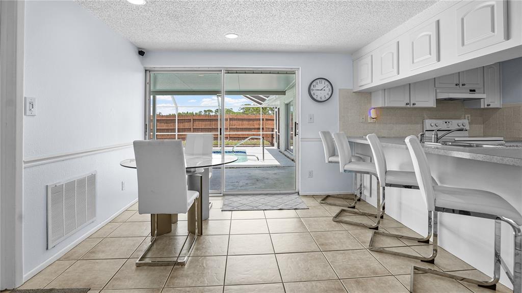 A dining area with tile floors, a glass table, and a kitchen breakfast bar — 8747 HEMLOCK LANE, PORT RICHEY, FL
