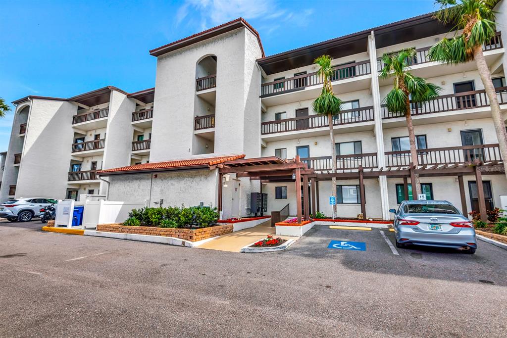 A multi-story apartment building exterior with a covered entrance, parking lot, and palm trees — 1602 STICKNEY POINT ROAD UNIT 404, SARASOTA, FL