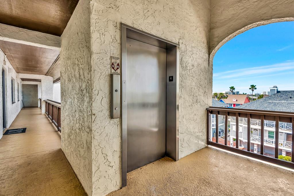 An outdoor hallway features a metal elevator door and a wooden railing overlooking a coastal neighborhood — 1602 STICKNEY POINT ROAD UNIT 404, SARASOTA, FL
