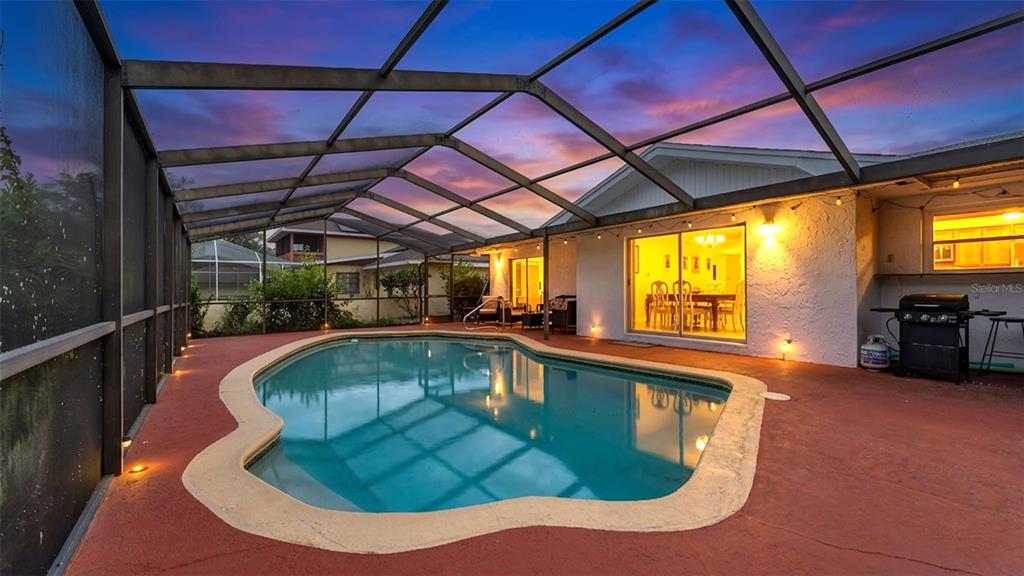 A screened-in patio features a swimming pool with a red deck and exterior lighting — 13 SUN AIR BOULEVARD E, HAINES CITY, FL