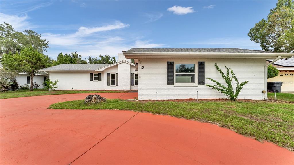 A white brick, single-story house features a large red circular driveway and a green lawn — 13 SUN AIR BOULEVARD E, HAINES CITY, FL