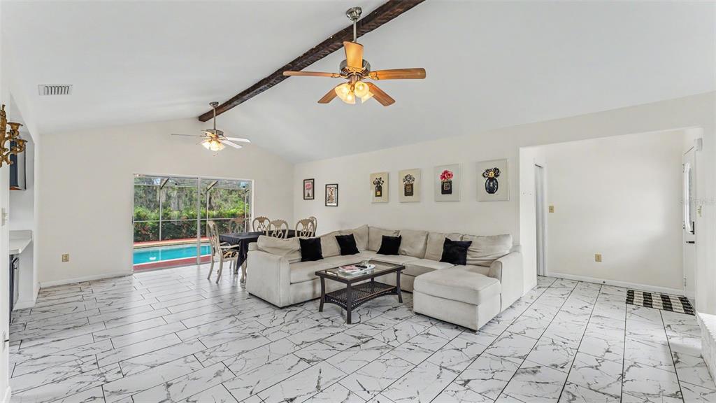 A living room with white marble-look tile floors, a sectional sofa, and a ceiling beam — 13 SUN AIR BOULEVARD E, HAINES CITY, FL