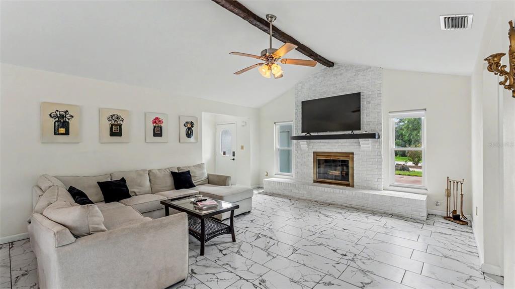 A living room features a white brick fireplace, marble-look tile flooring, and a vaulted ceiling — 13 SUN AIR BOULEVARD E, HAINES CITY, FL