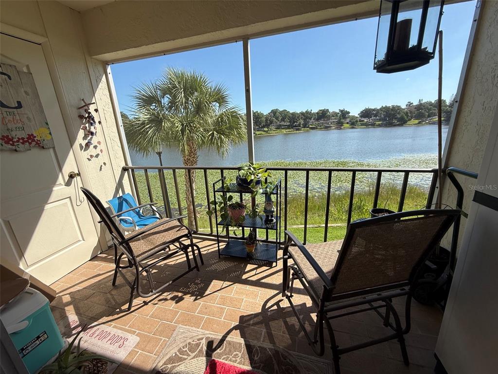 A screened-in balcony features two chairs, a plant stand, and a view of a lake — 410 E ORLANDO AVENUE UNIT 19A, OCOEE, FL