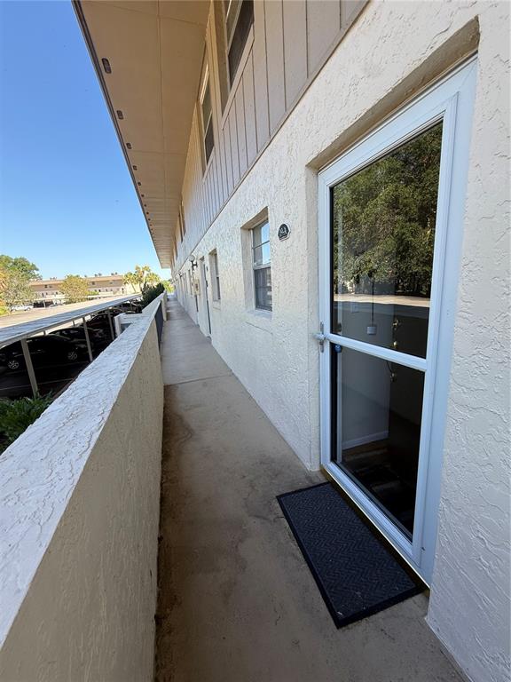 An exterior view of an apartment building walkway with a glass storm door and balcony — 410 E ORLANDO AVENUE UNIT 19A, OCOEE, FL