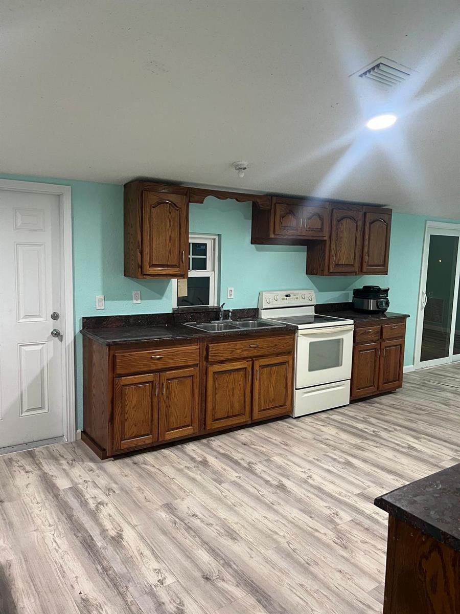 A kitchen features wood cabinets, dark countertops, a white stove, and light blue walls — 20480 NW 294th Street, Okeechobee FL 34972, OKEECHOBEE, FL