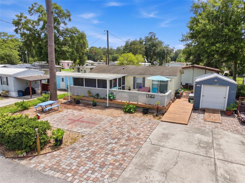 A yellow mobile home features a screened porch, a paver patio, and a detached storage shed — 2092 CULBREATH ROAD UNIT A42, BROOKSVILLE, FL