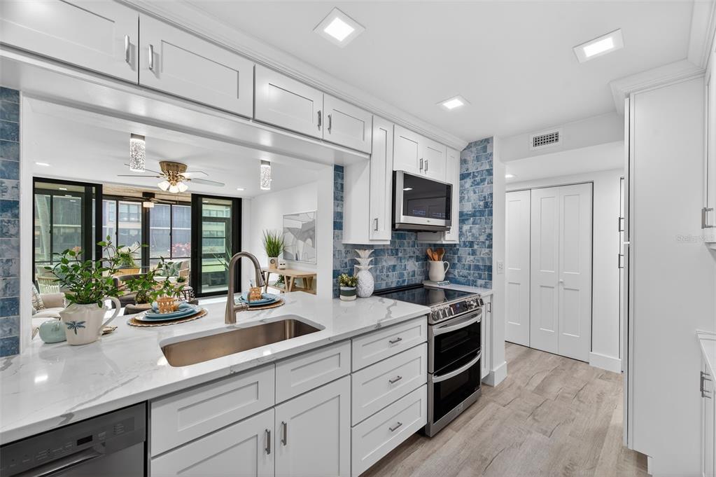 A white kitchen with quartz countertops, a stainless steel sink, and blue tiled backsplash — 19701 GULF BOULEVARD UNIT 120, INDIAN SHORES, FL