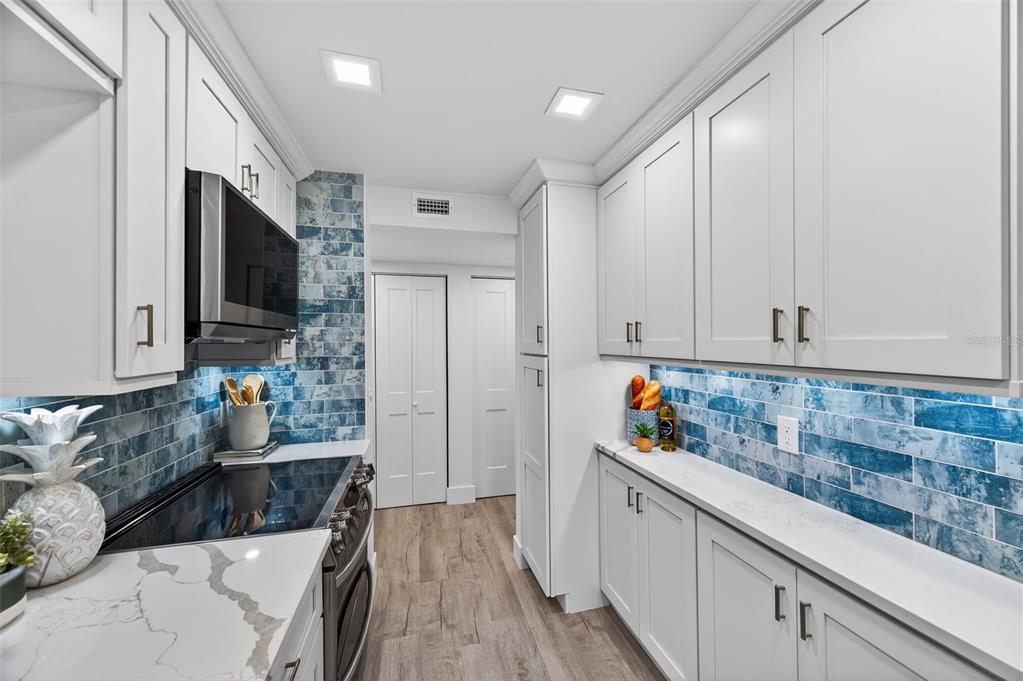 A galley kitchen features white cabinets, blue subway tile backsplash, and quartz countertops — 19701 GULF BOULEVARD UNIT 120, INDIAN SHORES, FL