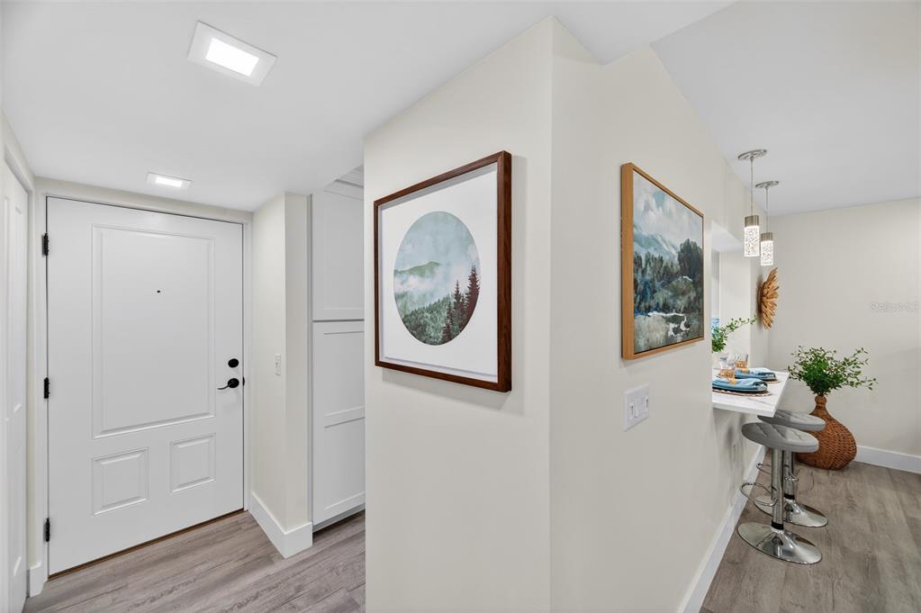 An entryway leads to a kitchen breakfast bar with two stools and wall art — 19701 GULF BOULEVARD UNIT 120, INDIAN SHORES, FL